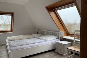 Ein Schlafzimmer mit schrägem Dach, einem Bett, einem Schreibtisch und zwei Fenstern.