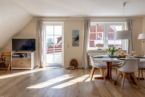 Ein modernes Wohnzimmer mit Fernseher, Essbereich und großen Fenstern.