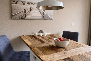 A dining area with a wooden table, a bowl of fruit, and a pendant light. - Oland in the house Achter de Dünen (Sankt Peter-Ording)