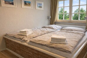 A double bed with a wooden headboard, a window with curtains, and three framed pictures on the wall. - Oland in the house Achter de Dünen (Sankt Peter-Ording)