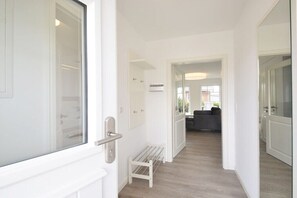 Ein Flur mit einer Bank, einer Tür, einer Wand-Klimaanlage und einem Blick in einen Wohnbereich mit einer Couch.