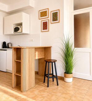A kitchen with a wooden island, a bar stool, a potted plant, and framed artwork on the wall. - Charming gîte in the heart of a Norman village (Mathieu)