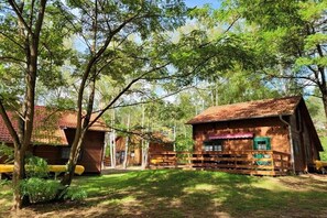 Eine rustikale Holzhütte mit Veranda und einem von Bäumen umgebenen, eingezäunten Garten.