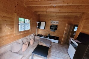 Ein Holzblockhaus-Innenraum mit einer Couch, einem kleinen Tisch, einer Lampe und einem Fernseher.