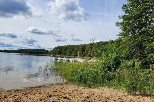 Ein See mit Booten, einem Sandstrand und üppiger Vegetation.