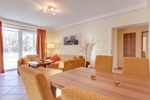 Ein modernes Wohnzimmer mit einem Holzesstisch, bequemen Sofas, einem Couchtisch und einem großen Fenster mit Vorhängen.