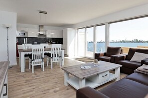 Ein modernes Wohnzimmer mit einem Holztisch, einem braunen Sofa und einem Essbereich mit weißen Stühlen.