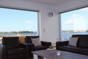 Ein Zimmer mit großem Fenster, einer Wanduhr und Blick auf ein Gewässer.