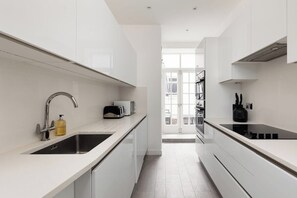 Una cocina moderna con armarios blancos, un lavamanos de acero inoxidable, una placa de inducción negra y un tostador.