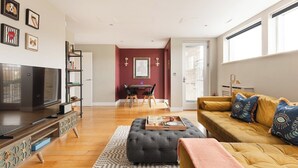Un salon comprenant un téléviseur, un canapé, un pouf et un coin repas avec des chaises et une table.