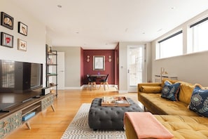 Ein Wohnzimmer mit Fernseher, Sofa, Hocker und einem Essbereich mit Stühlen und Tisch.