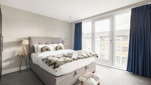 Une chambre avec un grand lit, une table de chevet, une lampe et une vue sur l’extérieur, accessible par une porte coulissante.
