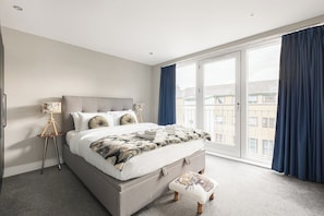 Ein Schlafzimmer mit einem großen Bett, einem Nachttisch, einer Lampe und Blick durch eine Schiebetür.