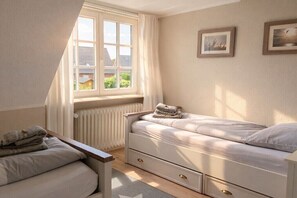 Ein Schlafzimmer mit zwei Betten, einem Fenster, einem Heizkörper und einem kleinen Tisch mit Handtüchern.