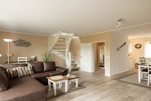 Ein Wohnzimmer mit einem braunen Ledersofa, einer weißen Treppe und einem Essbereich mit Tisch und Stühlen.