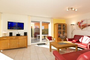 A modern living room with a television, wooden cabinet, red leather sofa, and a glass door leading to an outdoor area. - Holiday home with 4 bedrooms (Röbel\/Müritz)