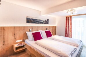 Ein Schlafzimmer mit einem hölzernen Kopfteil, zwei Betten, einem Nachttisch, einer Zeitschrift, einem Gemälde und einem Fenster mit Vorhängen.