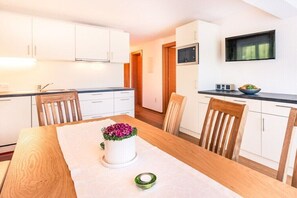 Eine moderne Küche mit weißen Schränken, einem Holztisch und einem an der Wand montierten Fernseher.