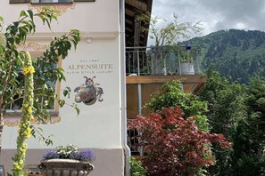 Ein Gebäude mit einem Schild, auf dem 'ALPENSUITE ALPIN STYLE LUXURY' steht, und einem Balkon mit Blick auf eine Berglandschaft.
