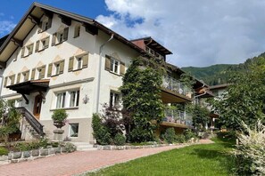Ein mehrstöckiges Gebäude im traditionellen Baustil, mit einer Treppe, die zum Eingang führt, und einem gepflegten Garten.