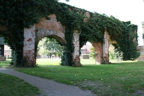 Eine alte Backsteinstruktur mit Bögen, dicht bewachsen mit Efeu, und ein Weg, der hindurchführt.