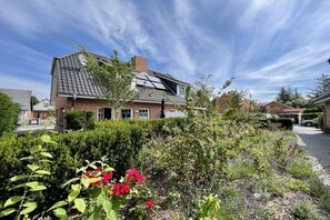 Ein Wohngebäude mit geneigtem Dach, Backsteinfassade und einem Garten mit blühenden Pflanzen.