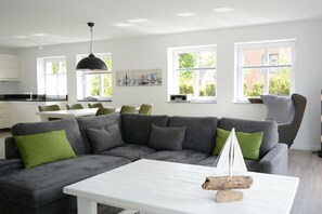 Ein modernes Wohnzimmer mit einem Ecksofa, einem weißen Couchtisch und einem Modell eines Segelboots.