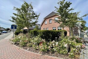 Ein Wohngebäude mit Backsteinfassade, einem gepflasterten Auffahrt und einem Garten mit blühenden Pflanzen.