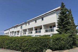 Ein mehrstöckiges Gebäude mit Balkonen, einer flachen Dachterrasse und einem Vorgarten.