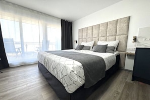 Ein modernes Hotelzimmer mit einem großen Bett, einem Kopfteil, einem kleinen Nachttisch und Blick auf einen Balkon.