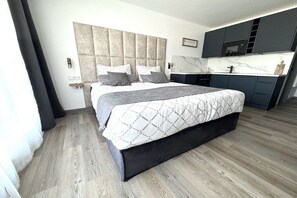 Ein modernes Schlafzimmer mit einem großen Bett, einer eingebauten Kopfteil und einer Küchenzeile mit dunklen Schränken und einer Marmorarbeitsplatte.
