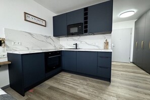 Une cuisine moderne avec des meubles de rangement aux couleurs sombres, un plan de travail en marbre, un four à micro-ondes encastré et un évier.