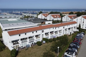 A modern building with a flat roof, multiple balconies, and a parking lot with cars.