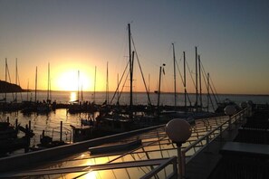 A marina with boats docked, a sunset in the background, and a railing with lights. - "The Coachman's Cottage" (Langballig)