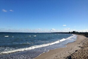 A beach with waves, a clear sky, and a distant shoreline. - "The Coachman's Cottage" (Langballig)
