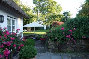 A white house with a thatched roof, a stone wall, and a garden with pink flowers and a lawn. - "The Coachman's Cottage" (Langballig)