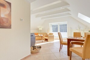 Ein modernes Wohnzimmer mit hohen Decken, einem Essbereich mit Tisch und Stühlen sowie einem großen Fenster, das für natürliches Licht sorgt.
