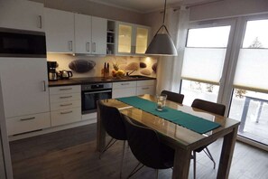 Eine moderne Küche mit weißen Schränken, einem Esstisch mit Stühlen und einem großen Fenster.