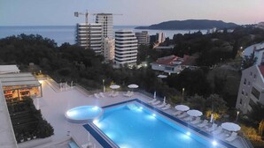 A rooftop swimming pool with lounge chairs and umbrellas, surrounded by buildings and a view of the sea. - Status M Apartments 98 (Becici)