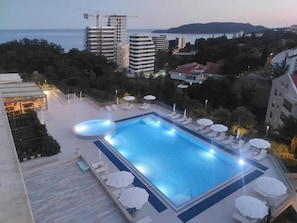 A rooftop swimming pool with lounge chairs and umbrellas, surrounded by buildings and a view of the sea. - Status M Apartments 98 (Becici)