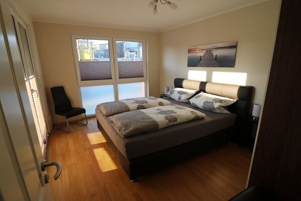 A bedroom with a bed, a chair, a window, and a painting on the wall.