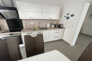 A modern kitchen with white cabinets, a built-in oven, and a dining area with a table and chairs.