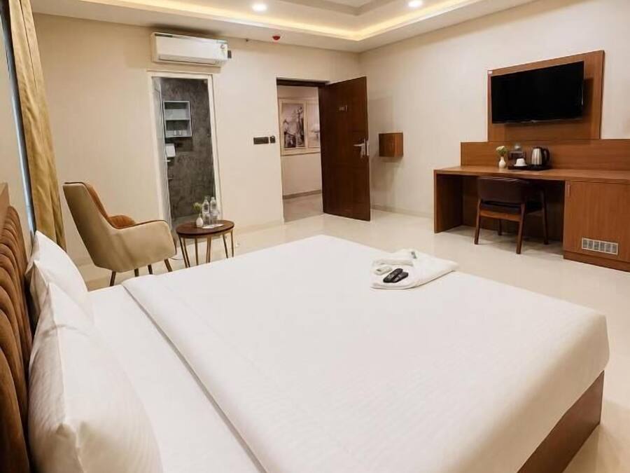 A hotel room with a bed, a desk, a chair, a television, and a small table.