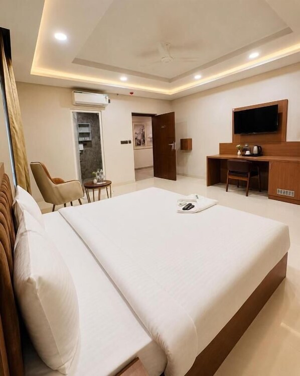 Habitación de hotel con cama, escritorio, silla, televisión y una pequeña mesa.
