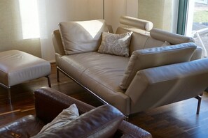 A modern living room with a beige sofa, a matching ottoman, and a patterned throw pillow. - Thatched House Four Seasons (Insel Poel)