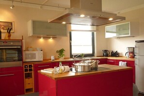 A modern kitchen with a central island, built-in oven, microwave, and a large window providing natural light. - Thatched House Four Seasons (Insel Poel)