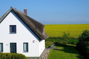 A white house with a thatched roof, a small garden, and a field in the background. - Thatched House Four Seasons (Insel Poel)