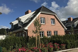 Ein Ziegelhaus mit geneigtem Dach, Satellitenschüssel und einem Garten mit rosa Blumen.