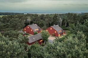 Ein großes Haus mit roter Fassade, umgeben von dichtem Wald, mit Blick auf ein Gewässer im Hintergrund.