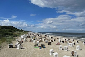 Ein Strand mit vielen weißen Strandhütten, einige davon mit Nummern, und einem grasbewachsenen Hügel im Hintergrund.